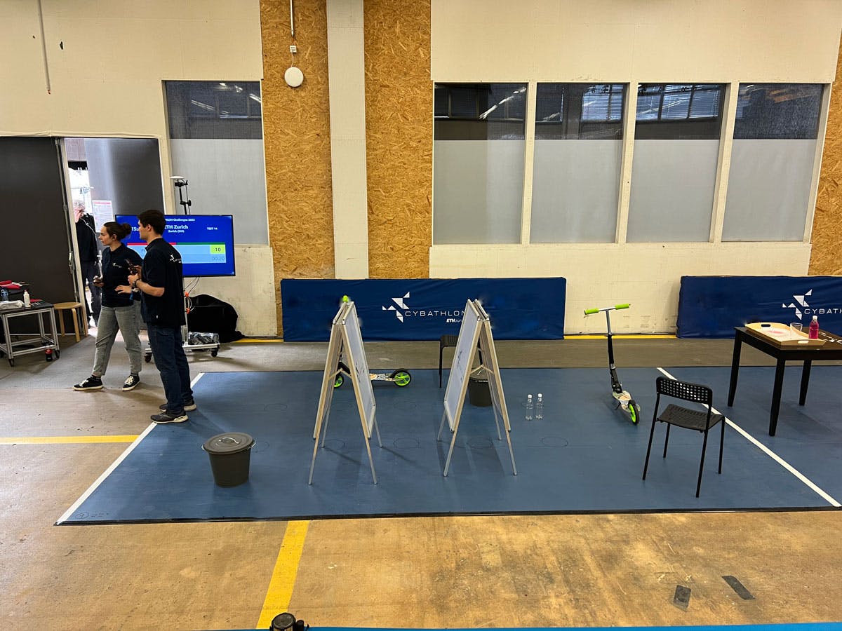 The image displays the setup for the 'Sidewalk' challenge in the Vision Assistance Race, featuring various obstacles and terrain changes designed to test the effectiveness of vision assistance technologies.