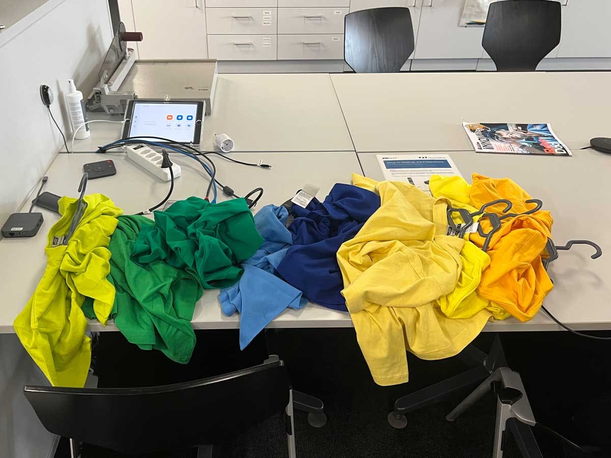 This image presents a table covered with an array of t-shirts in various colors, symbolizing the subject of Alexandru Top's challenge for the Cybathlon 2024 Vision Assistance Race. Each shirt represents a potential combination of color and brightness that the developed algorithm needs to recognize and sort correctly.